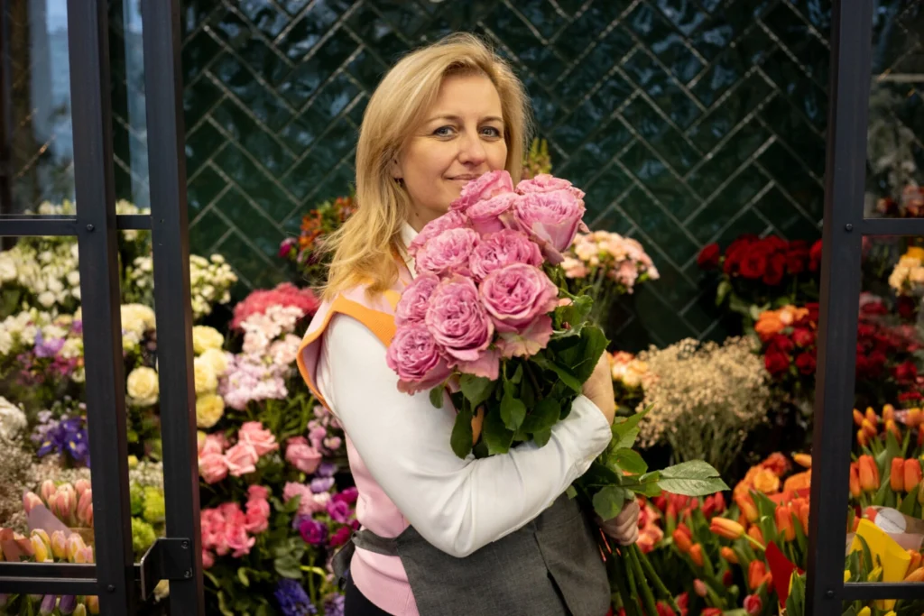 Właścicielka kwiaciarni trzyma bukiet róż wśród świeżych kwiatów. Zdjęcie przedstawia codzienną pracę przedsiębiorcy w branży florystycznej.